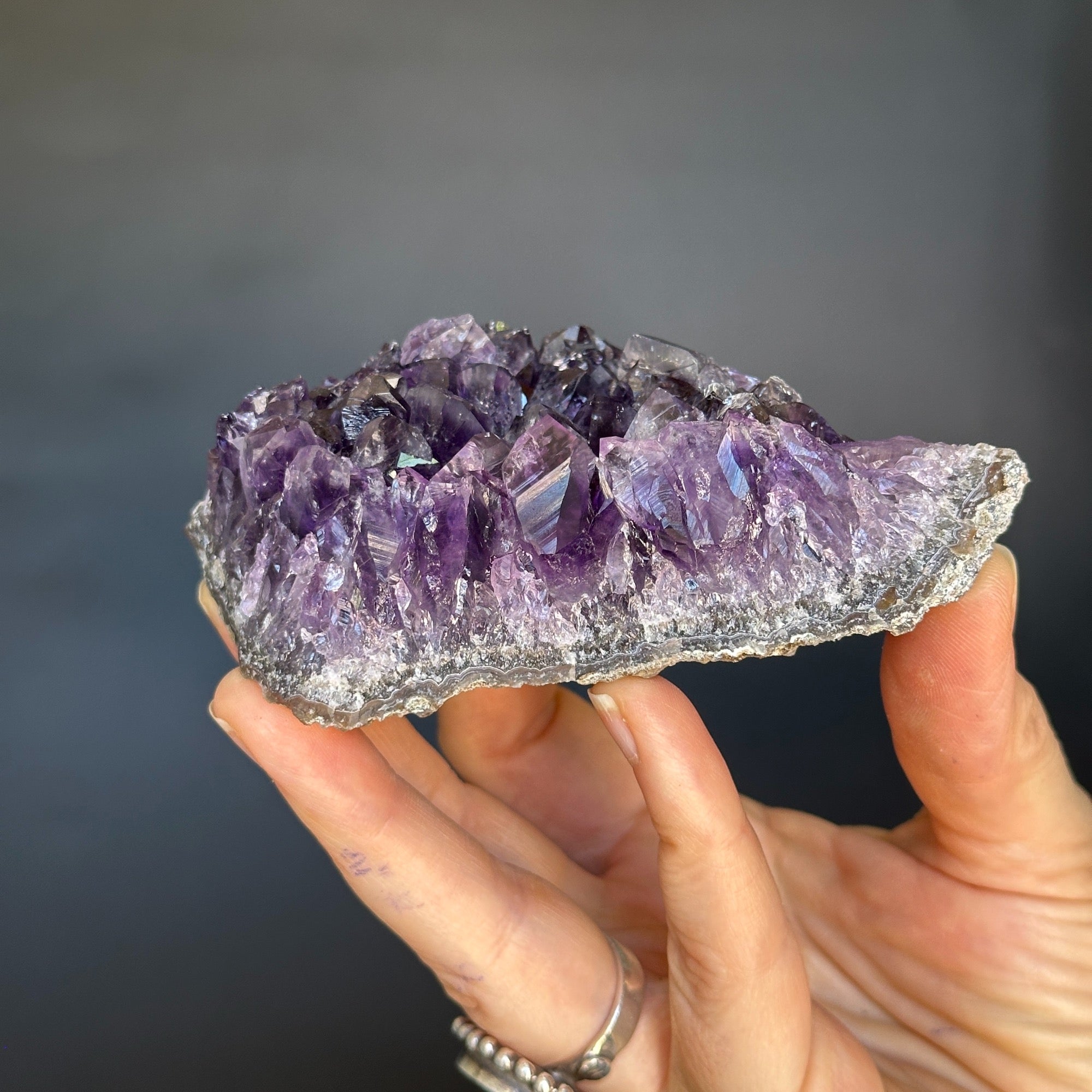 Hand holding a vibrant deep purple Uruguayan amethyst cluster with sparkling crystals.