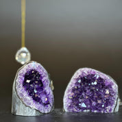 Two deep purple amethyst clusters with white agate layers, one on left with a crystal ornament.
