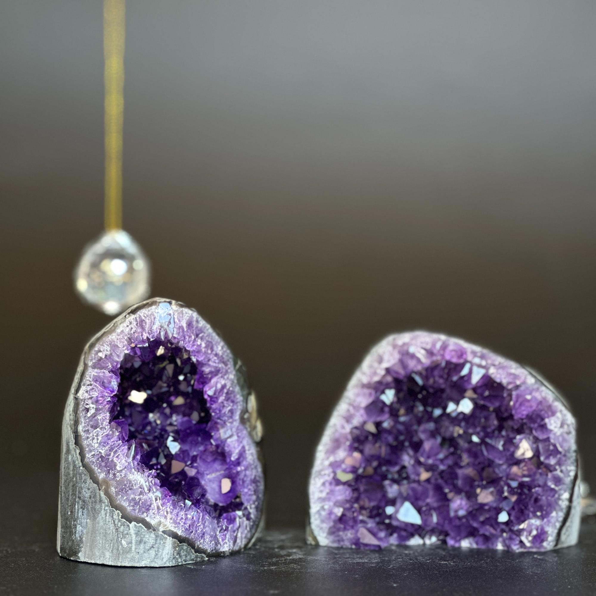 Two deep purple amethyst clusters with white agate layers, one on left with a crystal ornament.
