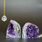 Two vibrant purple amethyst clusters with prominent agate layers on a dark surface.