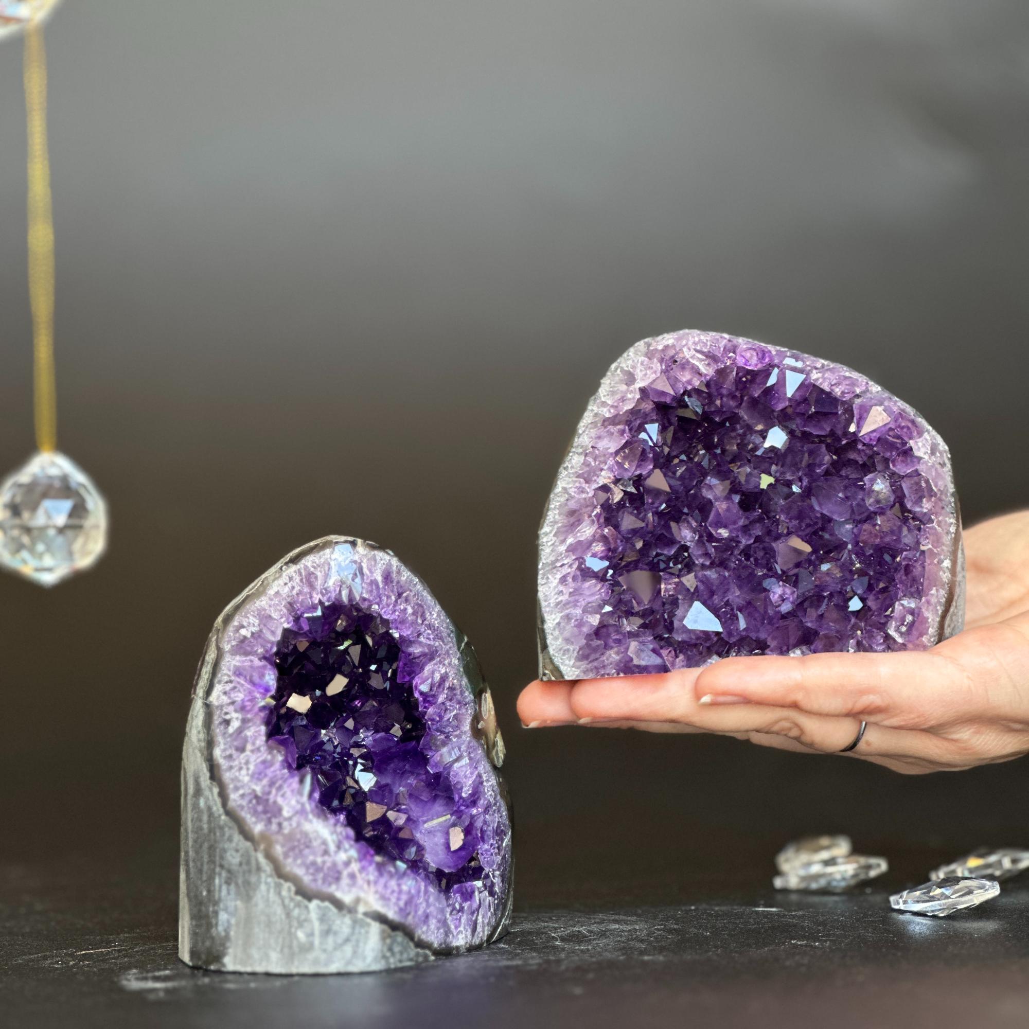 Two vibrant purple amethyst clusters with huge agate layers; one held in a hand, the other standing.