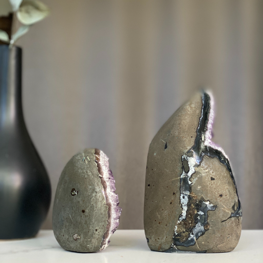 Two natural amethyst flame clusters with polished grey and green agate edges, next to a black vase.