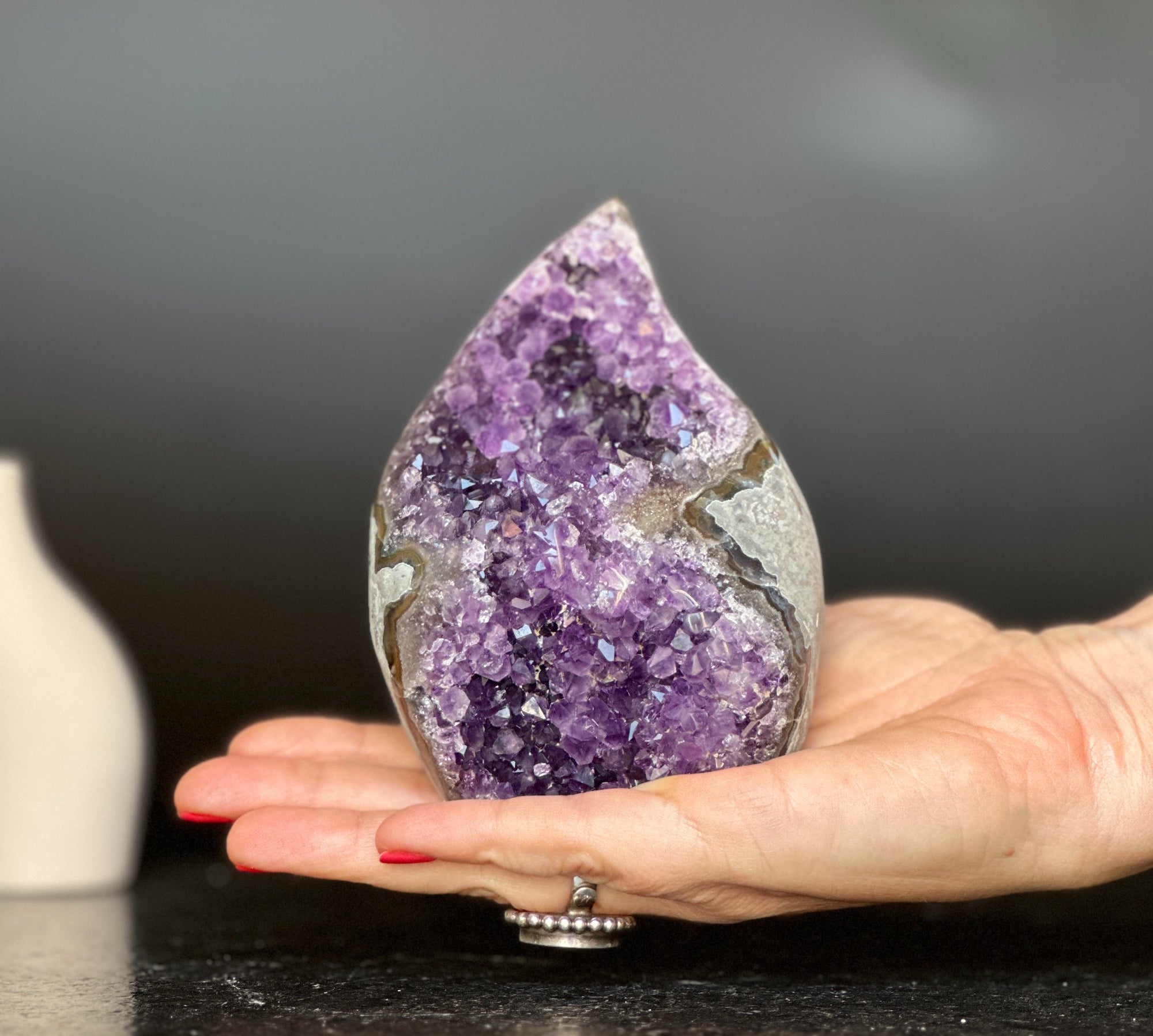 Polished amethyst flame geode with deep purple crystals and grey agate, held in a hand.