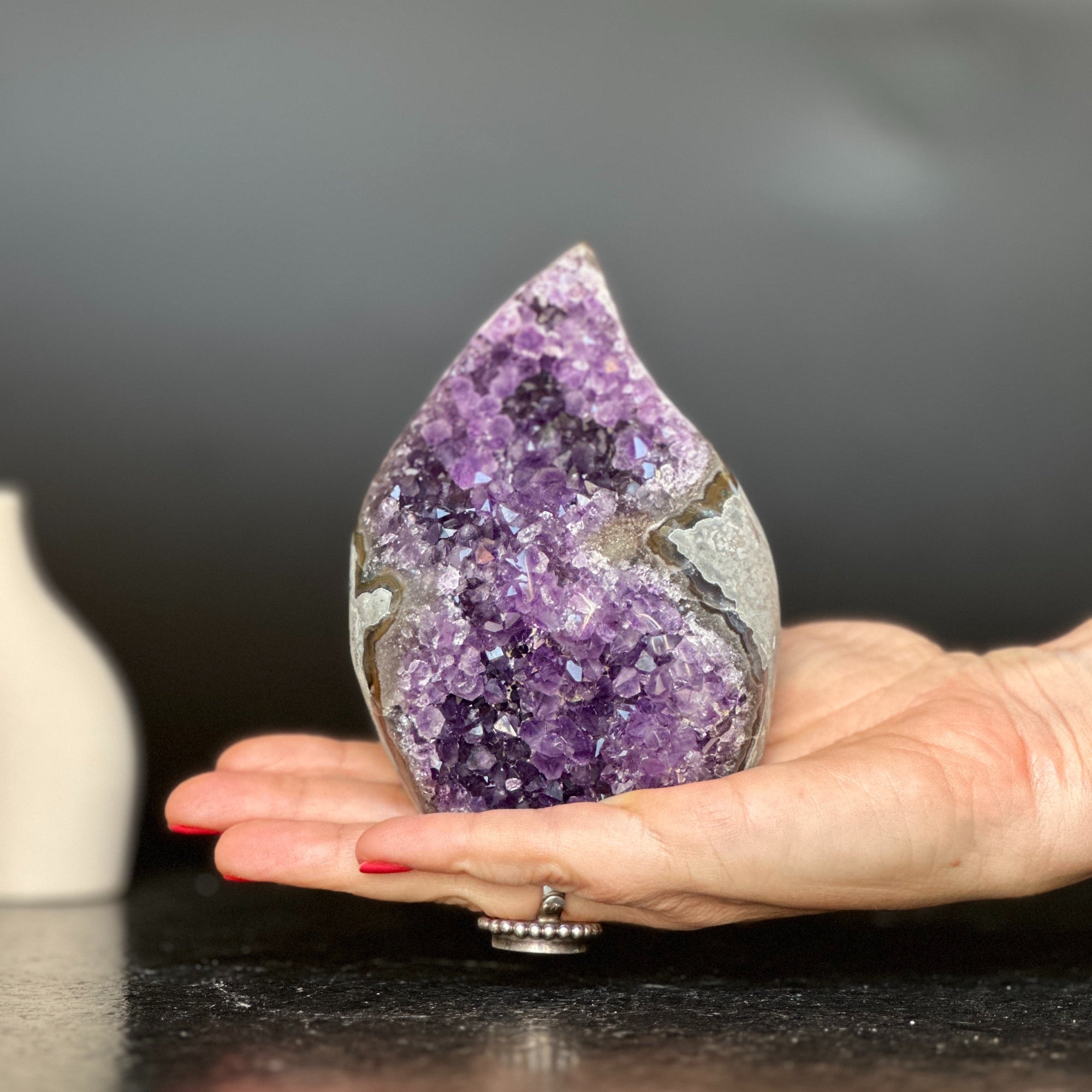 Polished amethyst flame geode with deep purple crystals and grey agate, held in a hand.