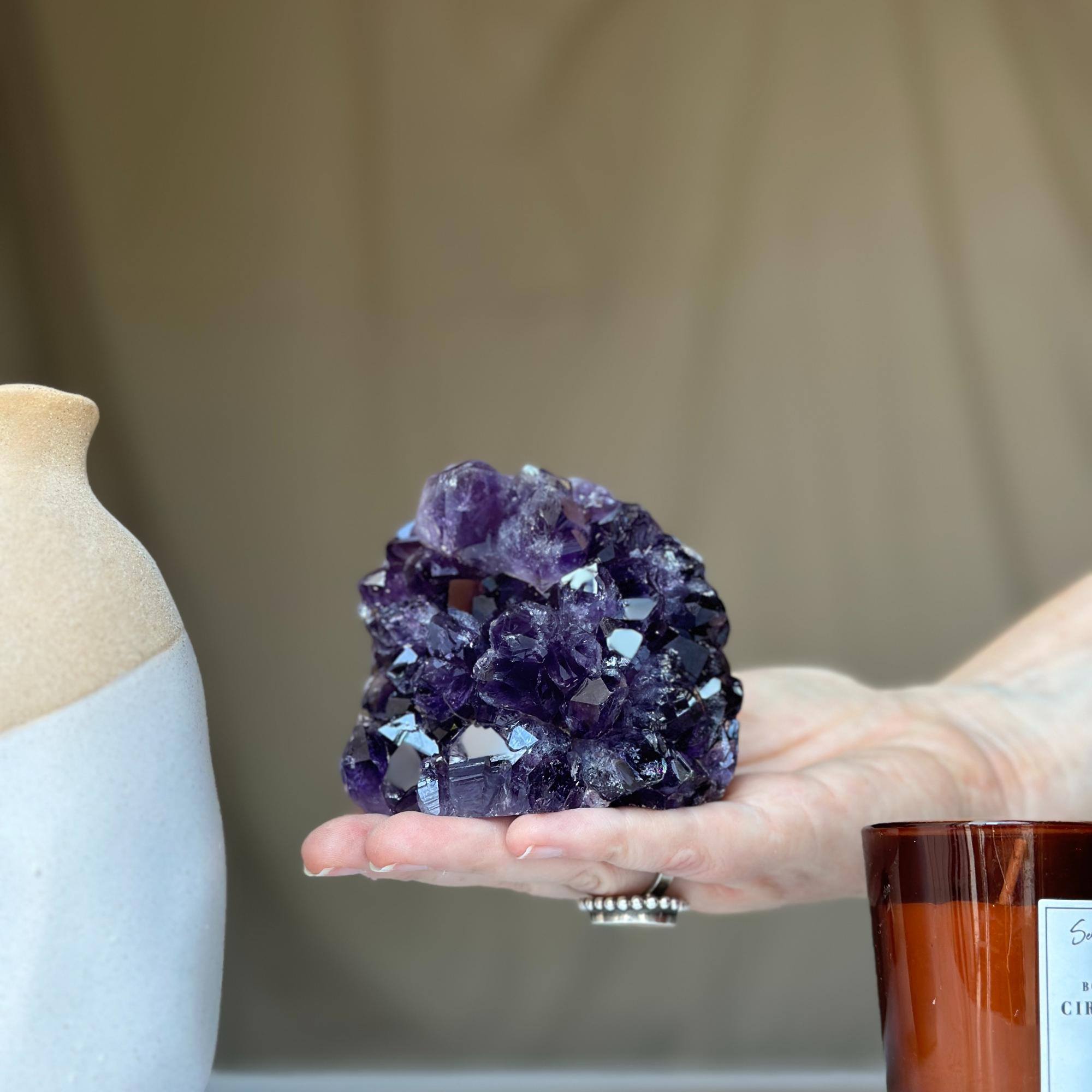 Large vibrant deep purple Uruguayan amethyst geode crystal cluster held in a hand.