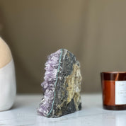 Vibrant deep purple Uruguayan amethyst geode cluster with raw rock exterior and unique agate layers.