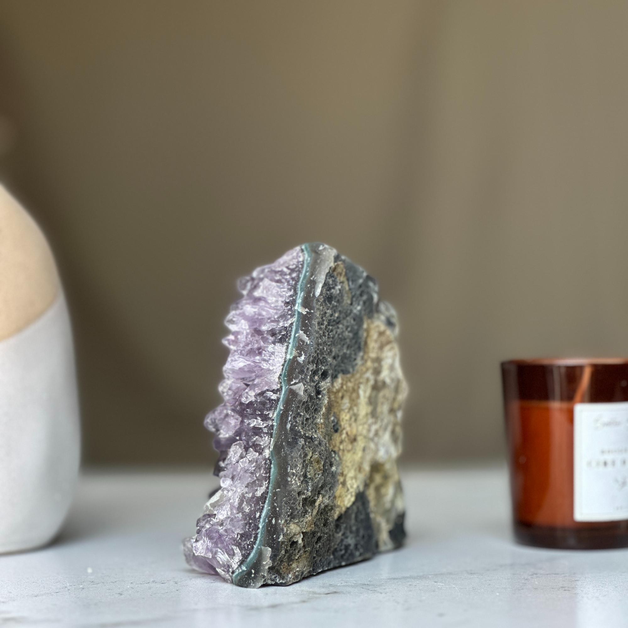 Vibrant deep purple Uruguayan amethyst geode cluster with raw rock exterior and unique agate layers.