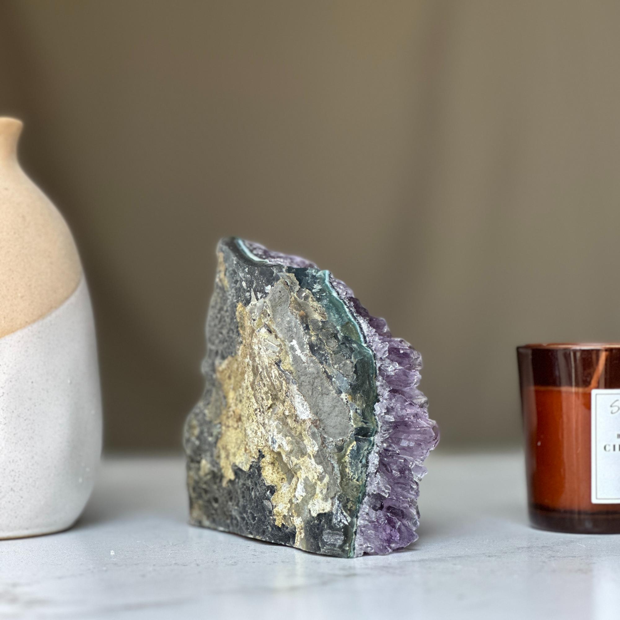 Deep purple amethyst geode crystal cluster with agate layers, next to a cream vase and brown candle.