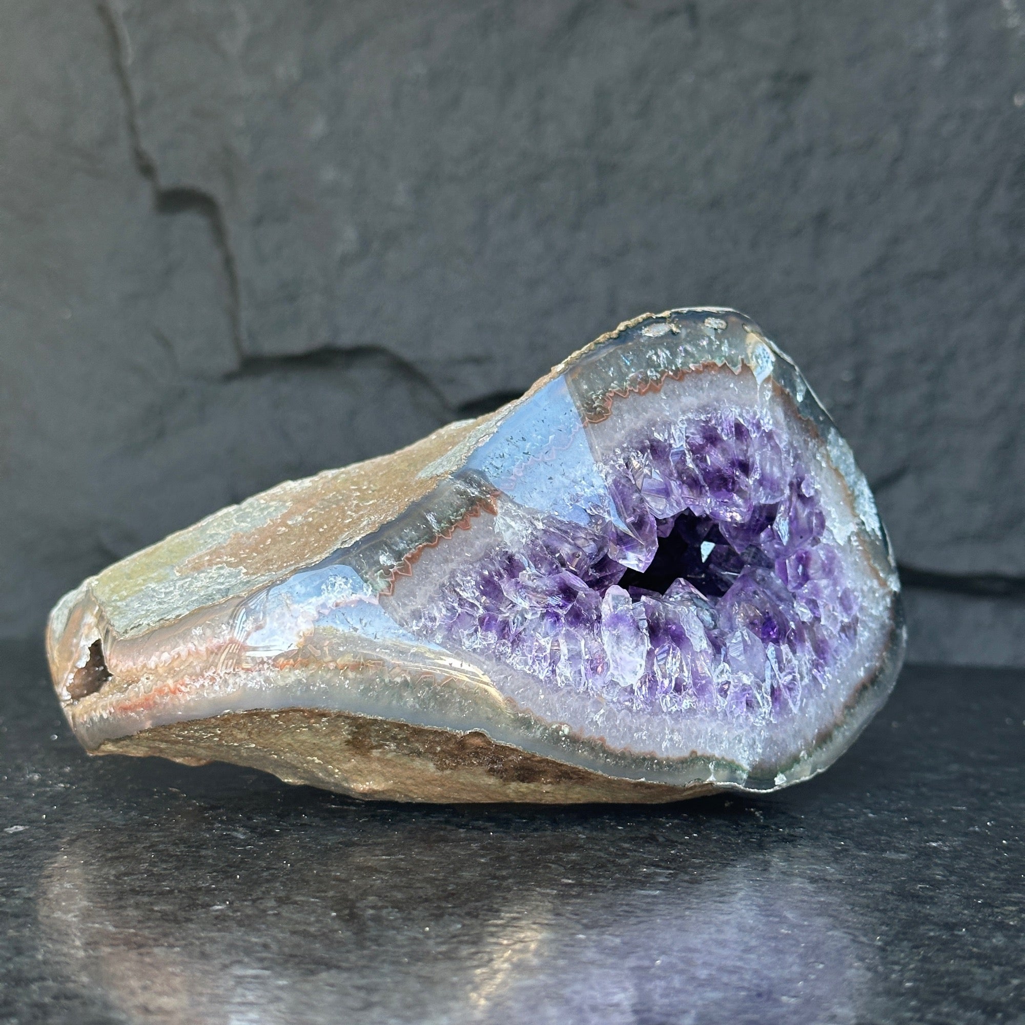 Self-standing amethyst geode featuring sparkling deep purple crystals within a natural gray-brown rock.