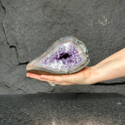 Vibrant purple Uruguayan amethyst geode held in hand, showcasing sparkling crystals. Measures 7x4 inches.