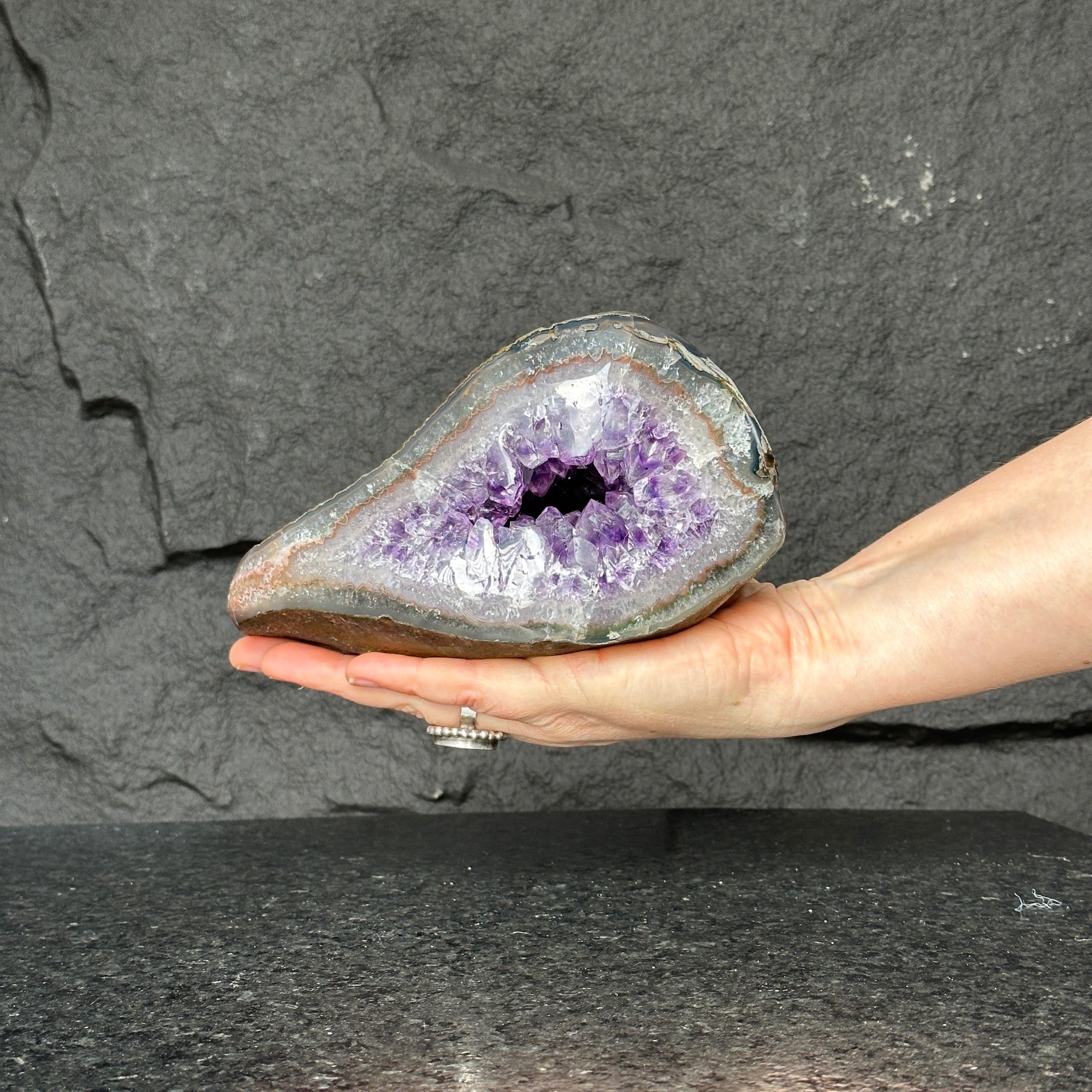 Vibrant purple Uruguayan amethyst geode held in hand, showcasing sparkling crystals. Measures 7x4 inches.