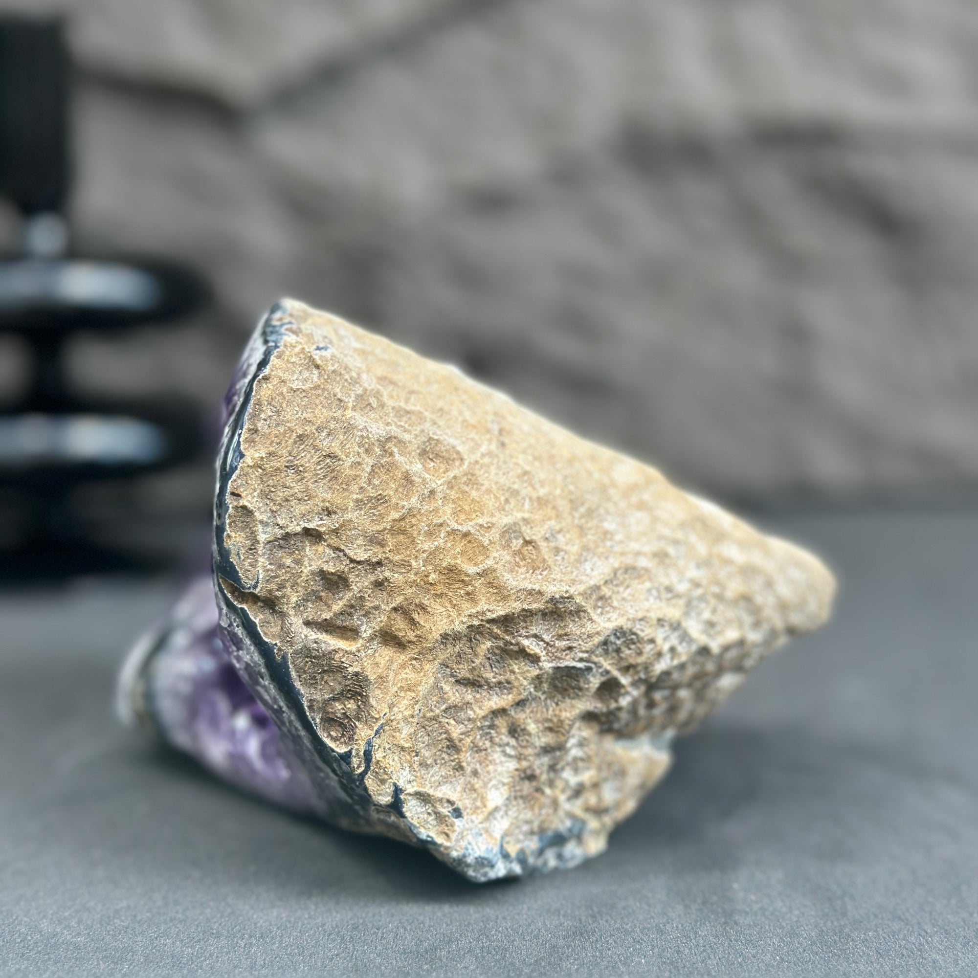 Rough, natural amethyst geode with deep purple crystals and a textured tan exterior.