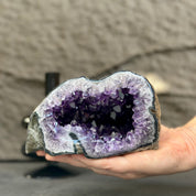 Hand holding a vibrant purple amethyst geode, showcasing its sparkling crystal interior and natural stone exterior.