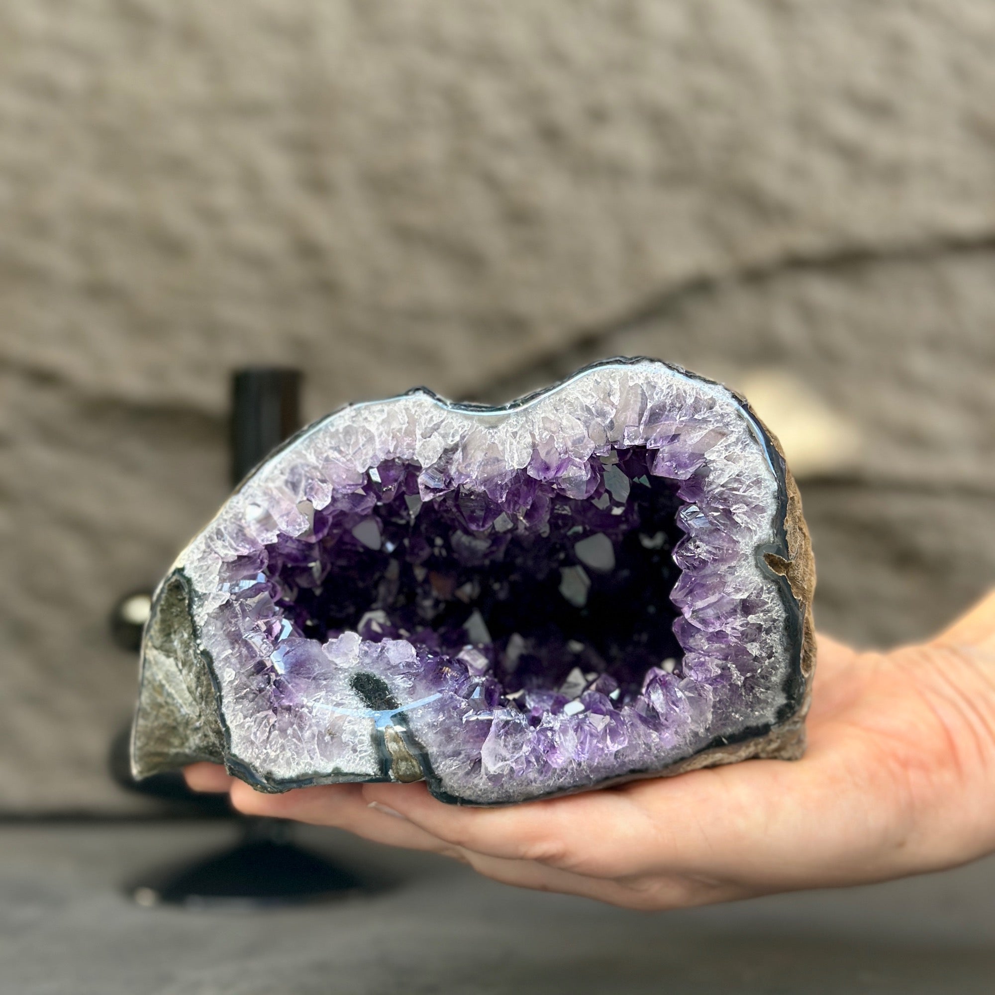 Hand holding a vibrant purple amethyst geode, showcasing its sparkling crystal interior and natural stone exterior.