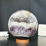 4-inch amethyst geode sphere with sparkling purple crystals and white quartz interior, resting on a round carob wood base.
