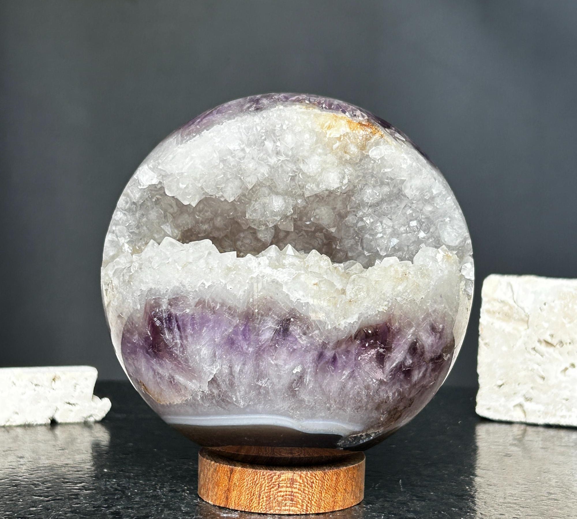4-inch amethyst geode sphere with sparkling purple crystals and white quartz interior, resting on a round carob wood base.