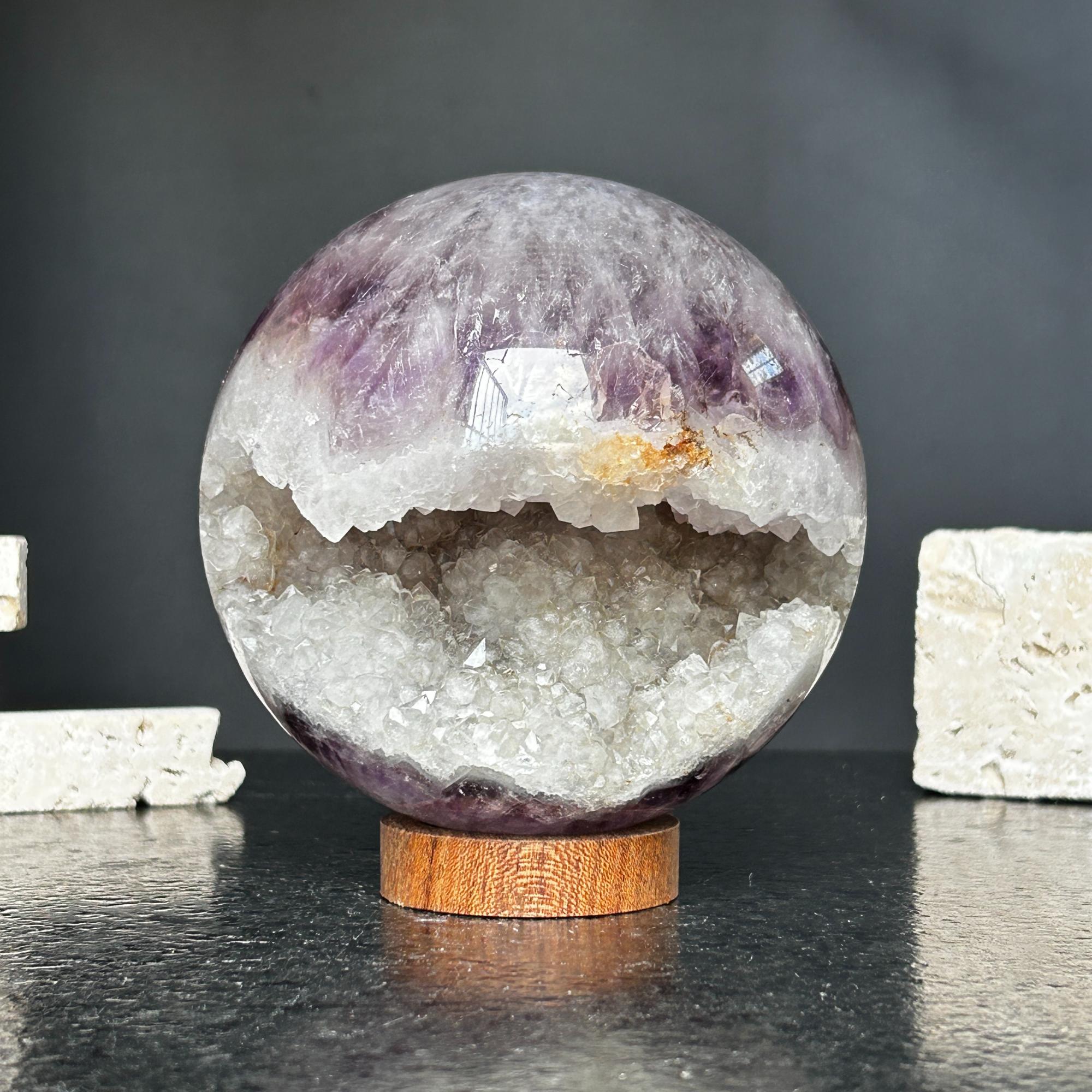 Polished amethyst crystal sphere geode, 4-inch diameter, showing deep purple and sparkling white druzy on a wood stand.