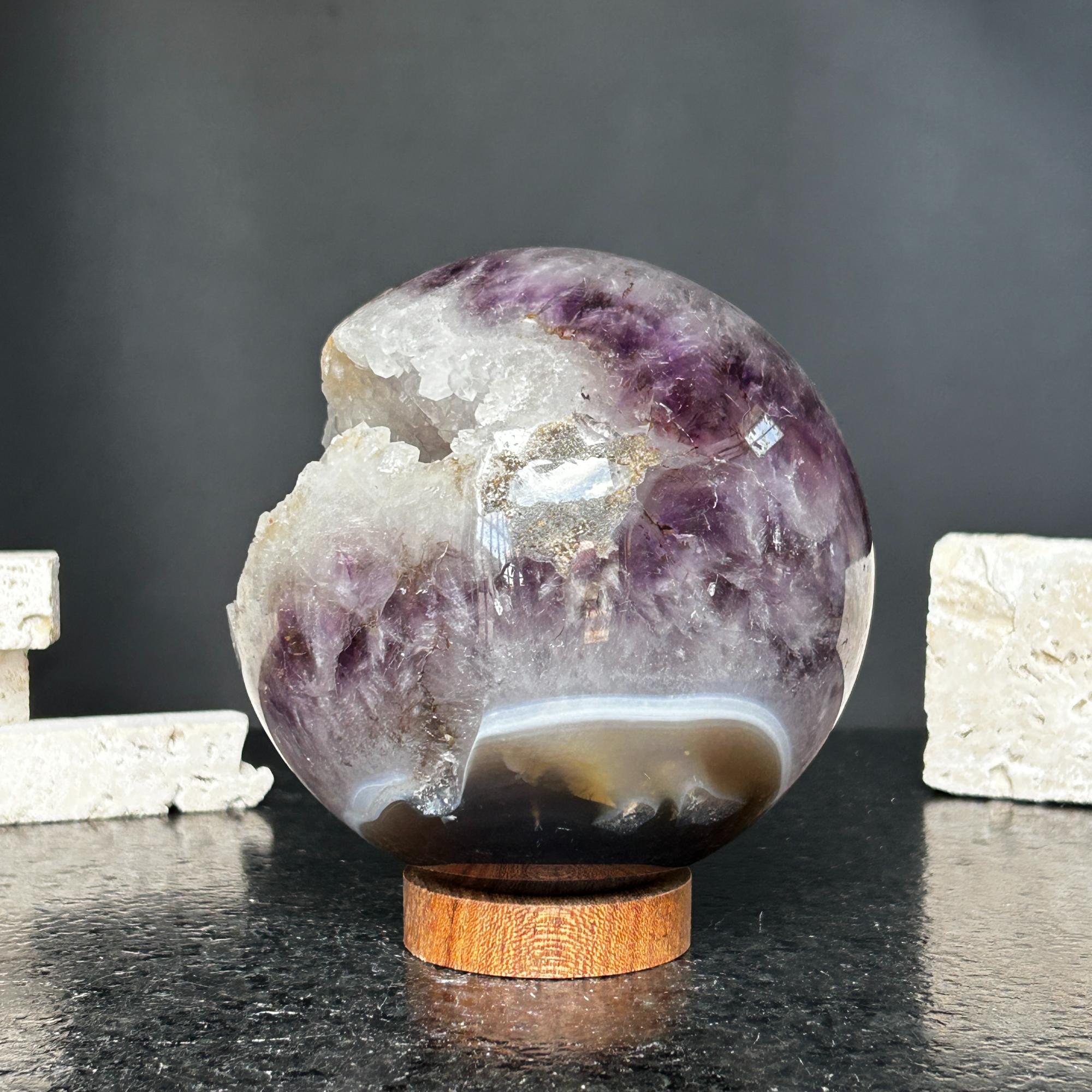 4-inch polished purple amethyst quartz crystal sphere with a raw white geode opening on a round carob wood base.