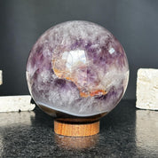 Polished amethyst quartz crystal sphere, 4-inch diameter, displaying natural purple and white patterns, on a carob wood base.