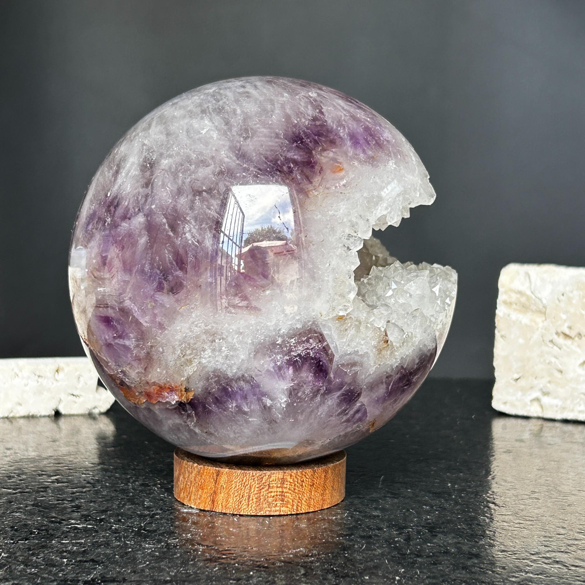 4-inch polished purple amethyst quartz crystal sphere with a sparkling white geode opening, on a round carob wood base.