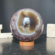 Polished amethyst quartz geode sphere with a white banded interior, displayed on a round carob wood base.