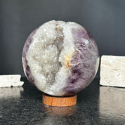 Purple amethyst quartz crystal sphere geode with sparkling white interior on a round wooden base.
