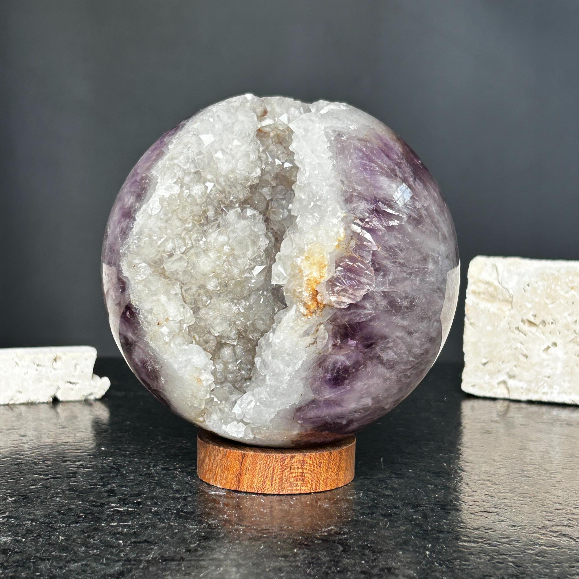 Purple amethyst quartz crystal sphere geode with sparkling white interior on a round wooden base.