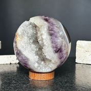 Polished amethyst quartz crystal sphere with a sparkling white geode interior on a round carob wood base.