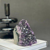Deep purple Uruguayan cathedral amethyst cluster, 4-inch raw stone, on a white book.