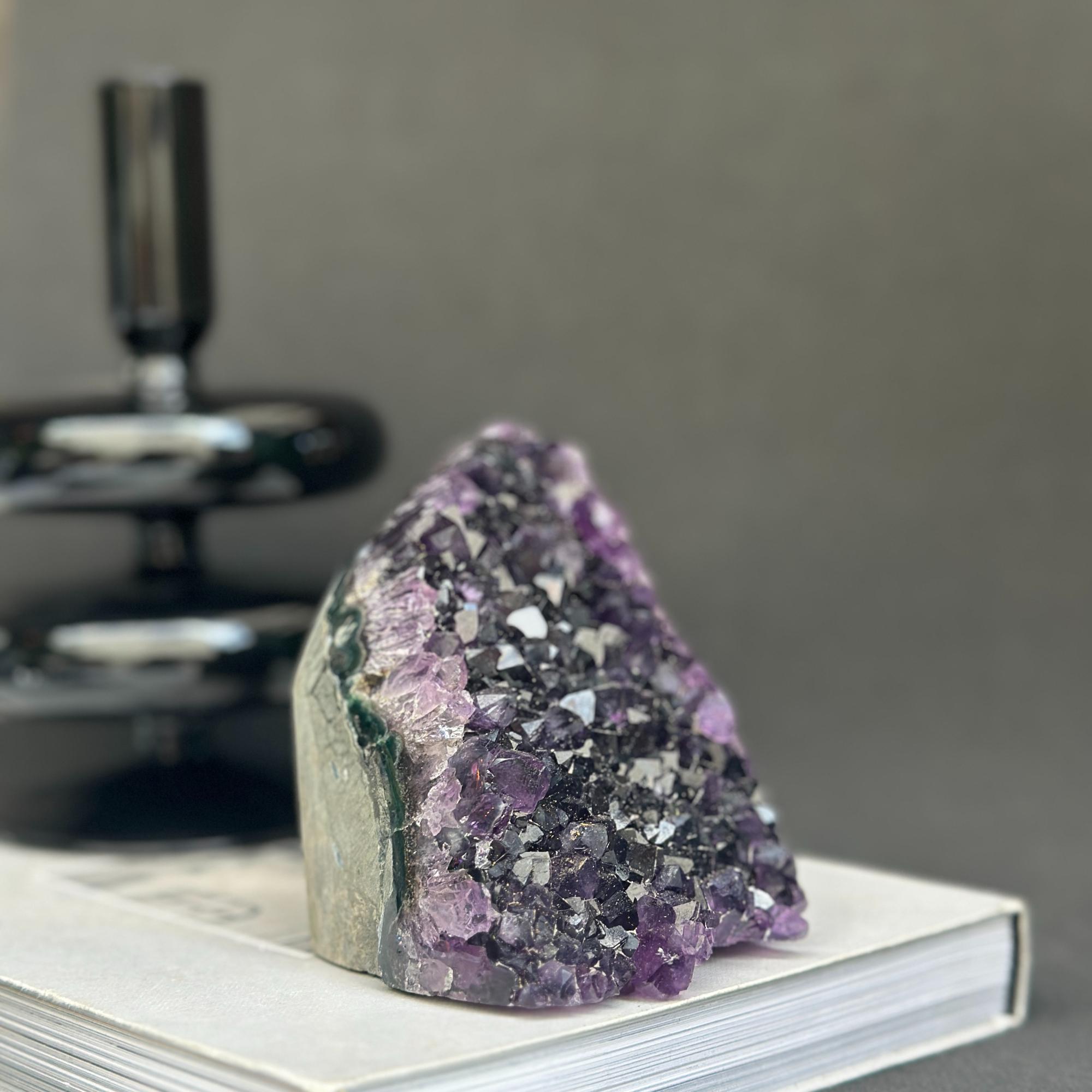 Deep purple Uruguayan cathedral amethyst cluster, 4-inch raw stone, on a white book.