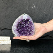 Uruguayan amethyst geode, 4.5" tall, with deep purple crystals and gray-green agate edges, held in a hand.