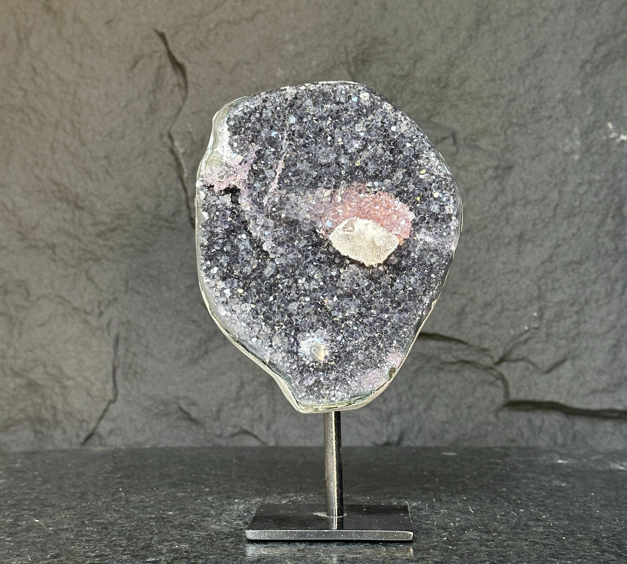 Dark purple amethyst geode with pink and white micro crystals on a sleek metal pedestal.