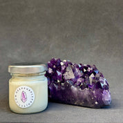 Small candle in a glass jar with a purple crystal formation on a gray background