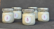 Five small jars with candles inside, each labeled with a circular sticker on a dark background.