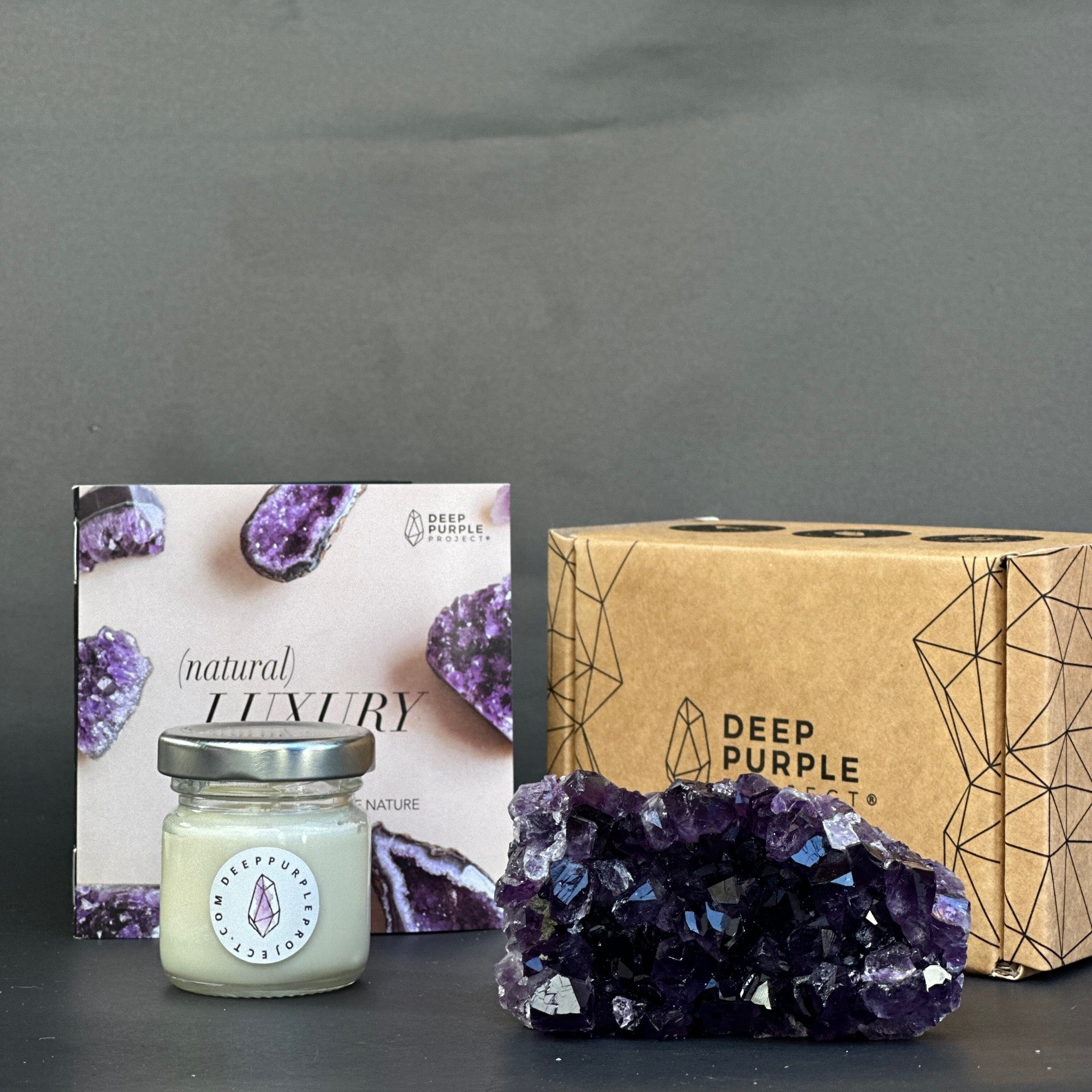 Candle, amethyst crystal, and packaging with 'Deep Purple' branding on a gray background