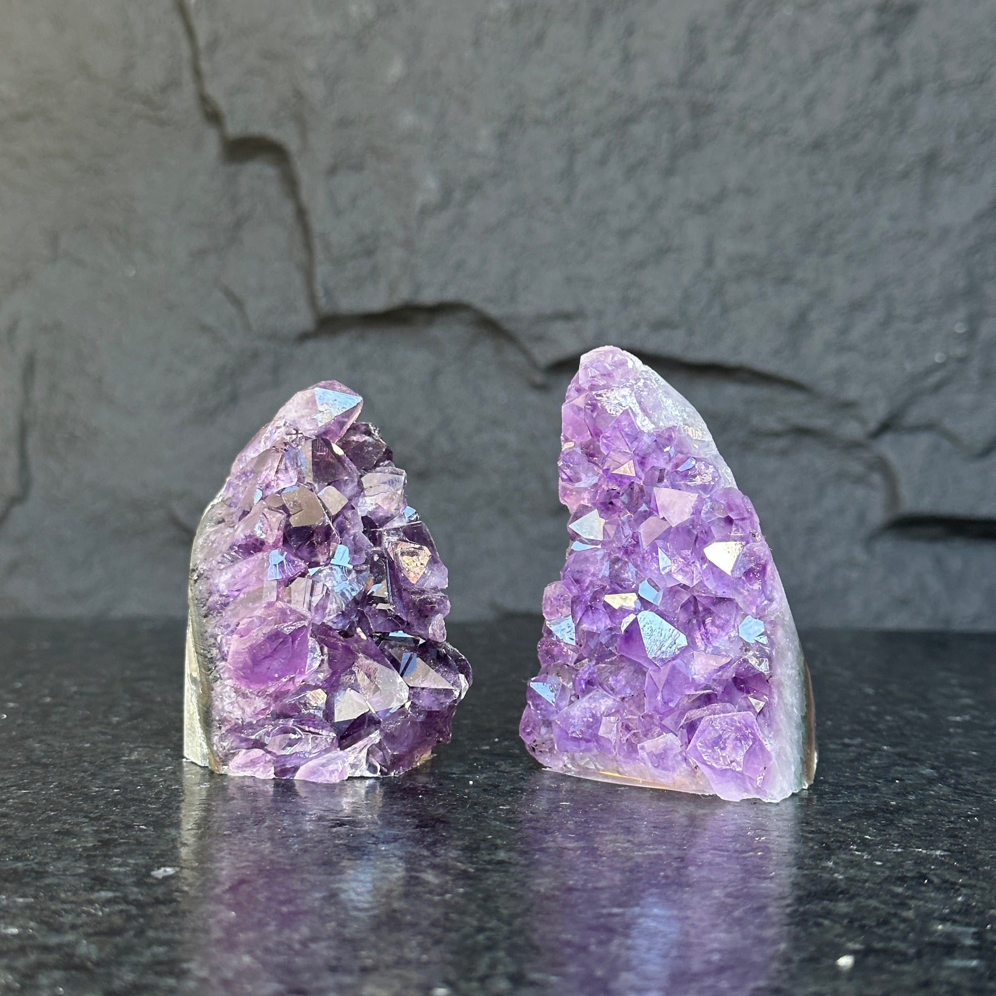 Two raw Uruguayan amethyst geode clusters, deep purple, 3-inch high, on a dark surface.