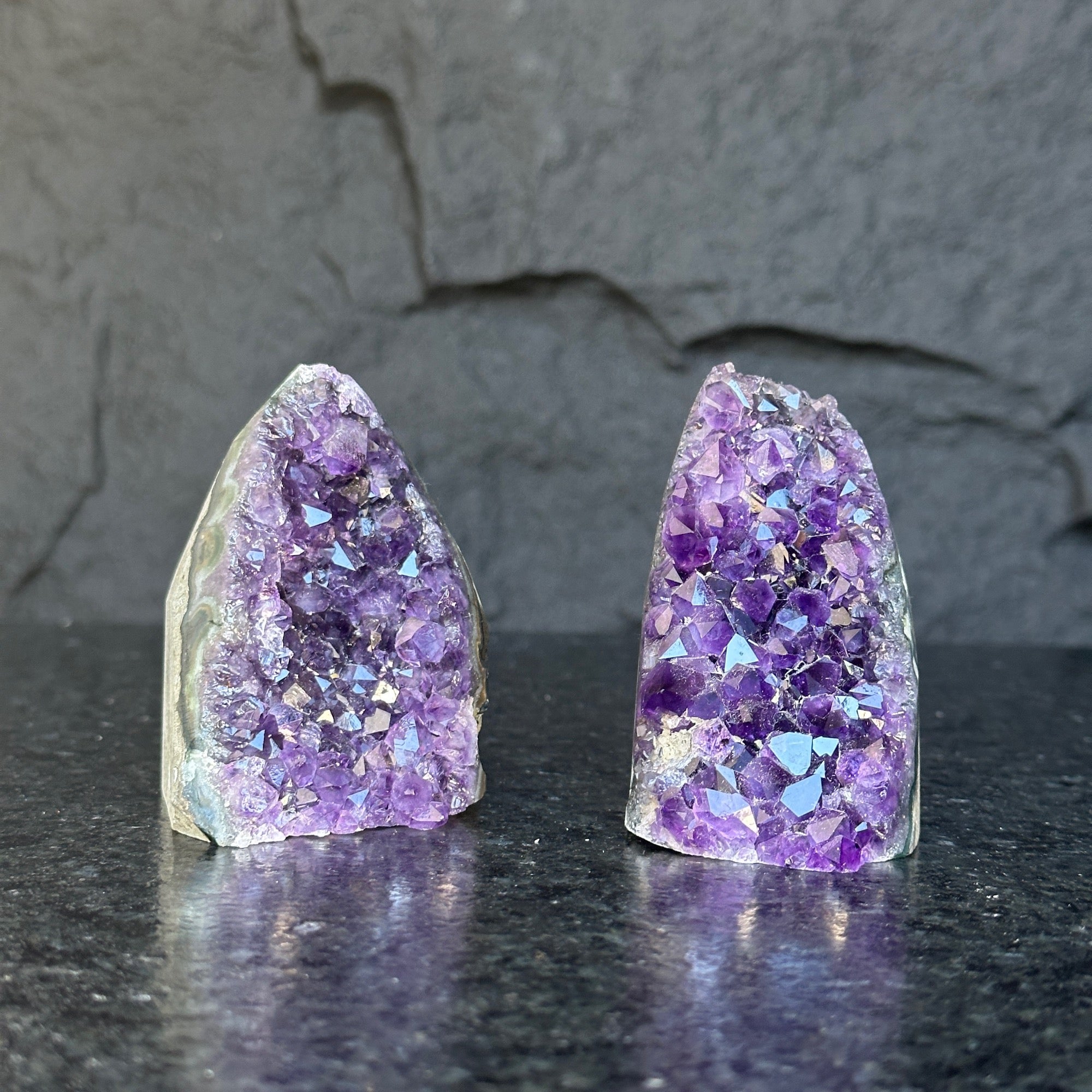 Two raw, deep purple Uruguayan amethyst geode clusters, 3-inch high, on a dark stone surface.