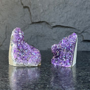 Two raw, deep purple Uruguayan amethyst geode clusters, 3-inch high, on a dark surface.