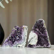 Two deep purple amethyst geodes with sparkling crystals and white calcite formations.
