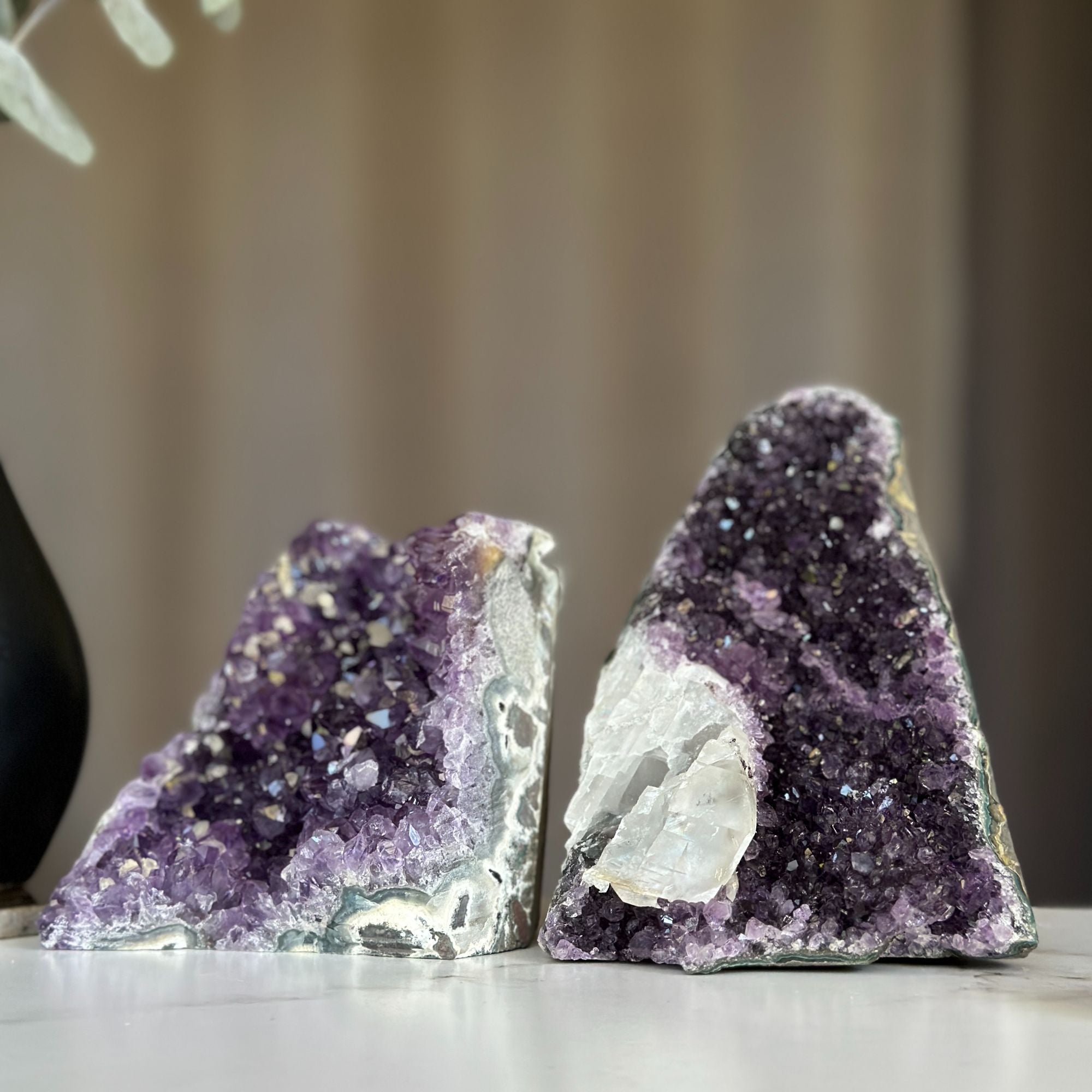 Two deep purple amethyst geodes with sparkling crystals and white calcite formations.