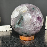 Large purple amethyst crystal sphere with green inclusions on a round wooden base.