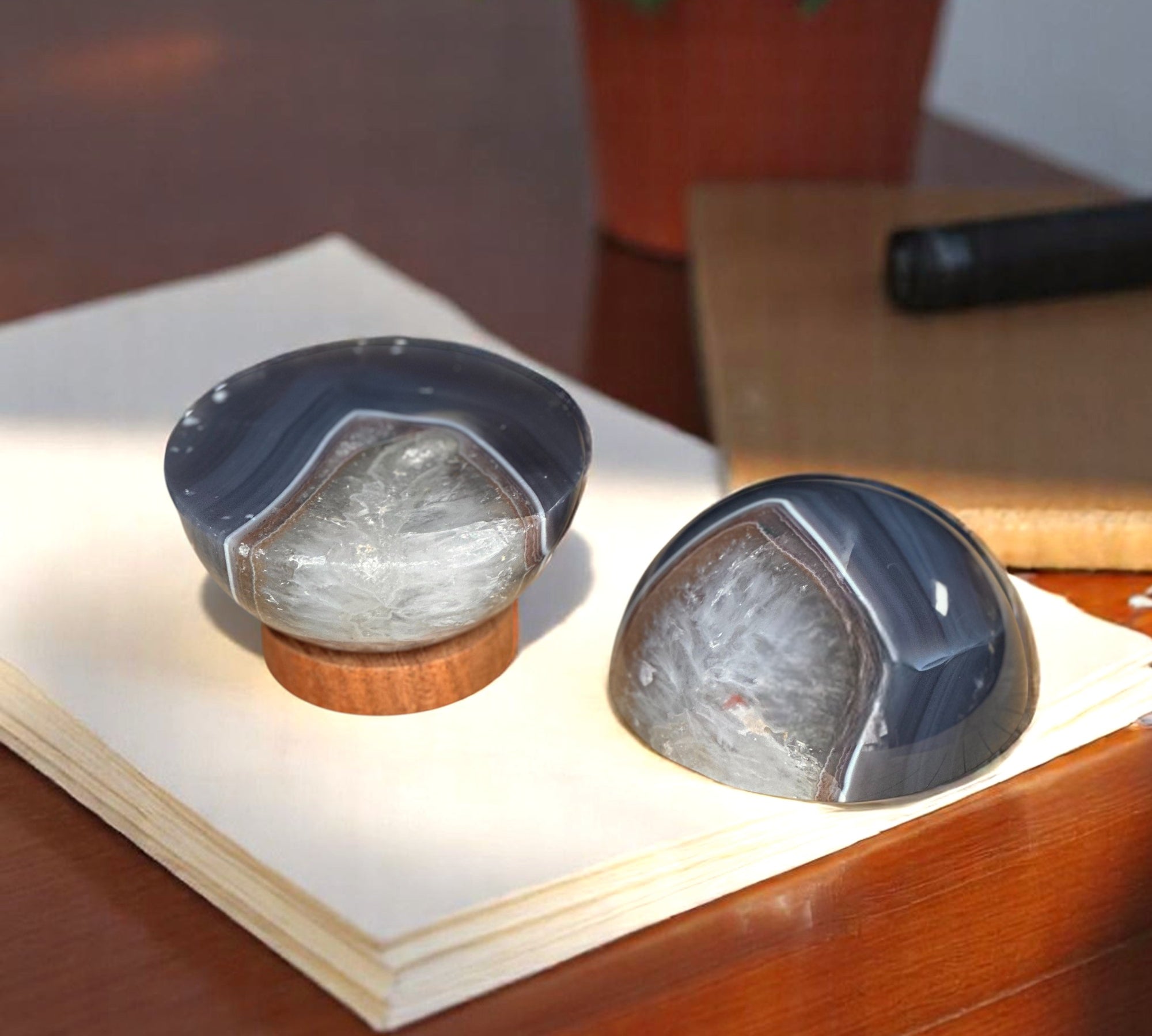 Two sphere-shaped agate paperweights on top of a wooden stand, placed on a desk next to a stack of papers.