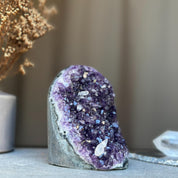 Deep purple amethyst stone geode cluster, sparkling violet crystals on a natural grey rock base.