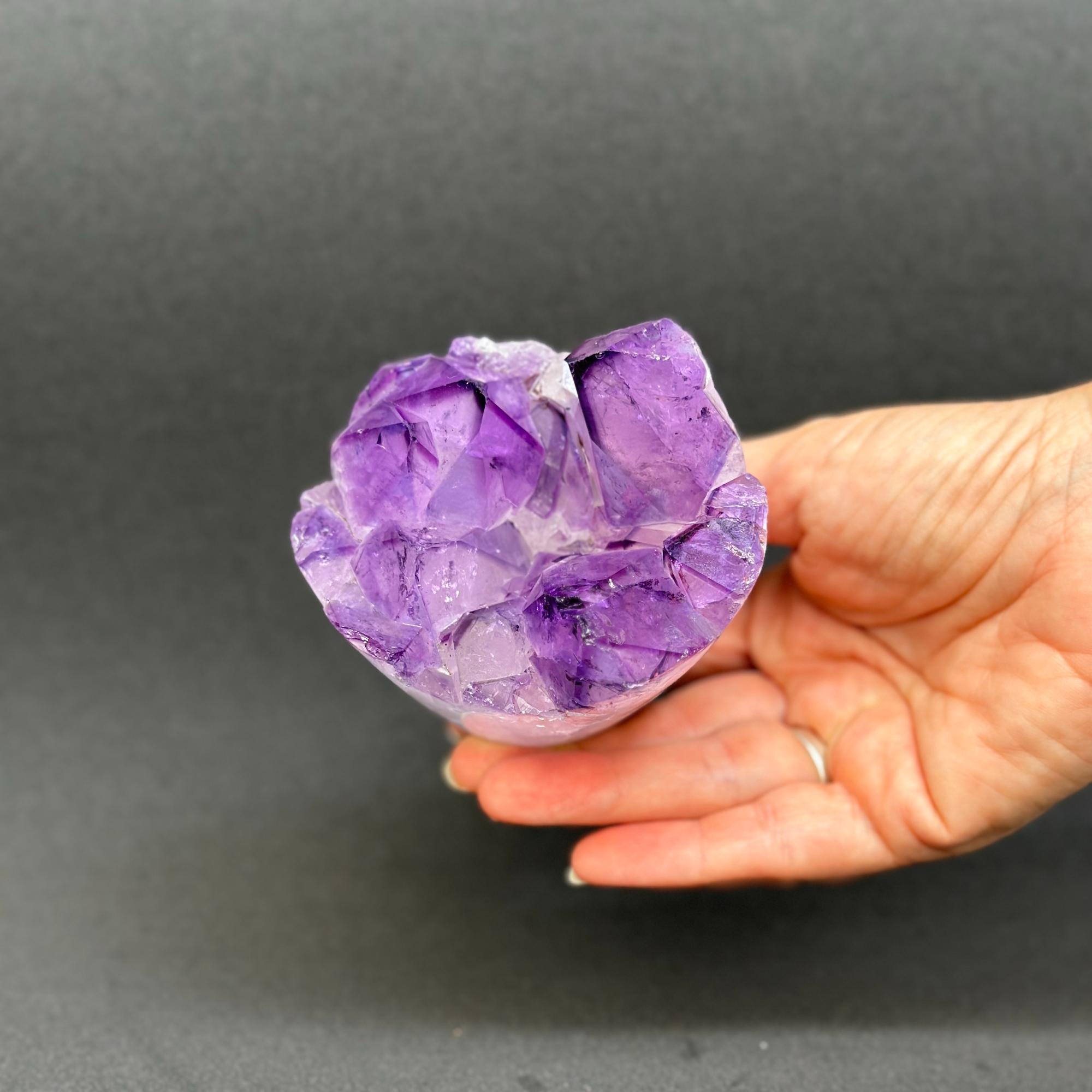 Top grade Uruguayan amethyst geode cluster with vibrant deep purple crystal points, held in a hand.