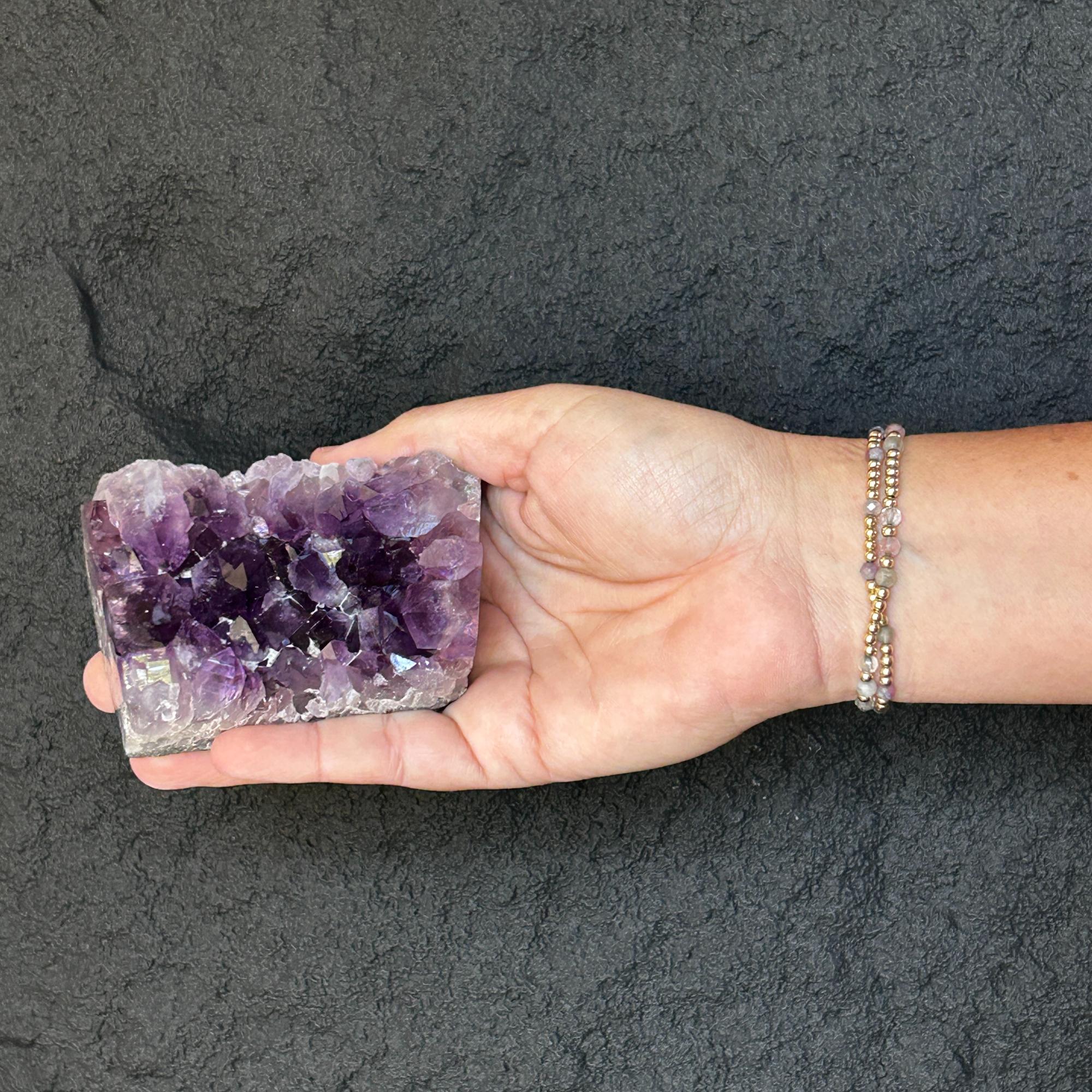 Hand holding a flat, raw Uruguayan amethyst crystal cluster with deep purple points.