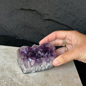 Hand holding a flat, vibrant deep purple Uruguayan amethyst crystal cluster with a raw base.