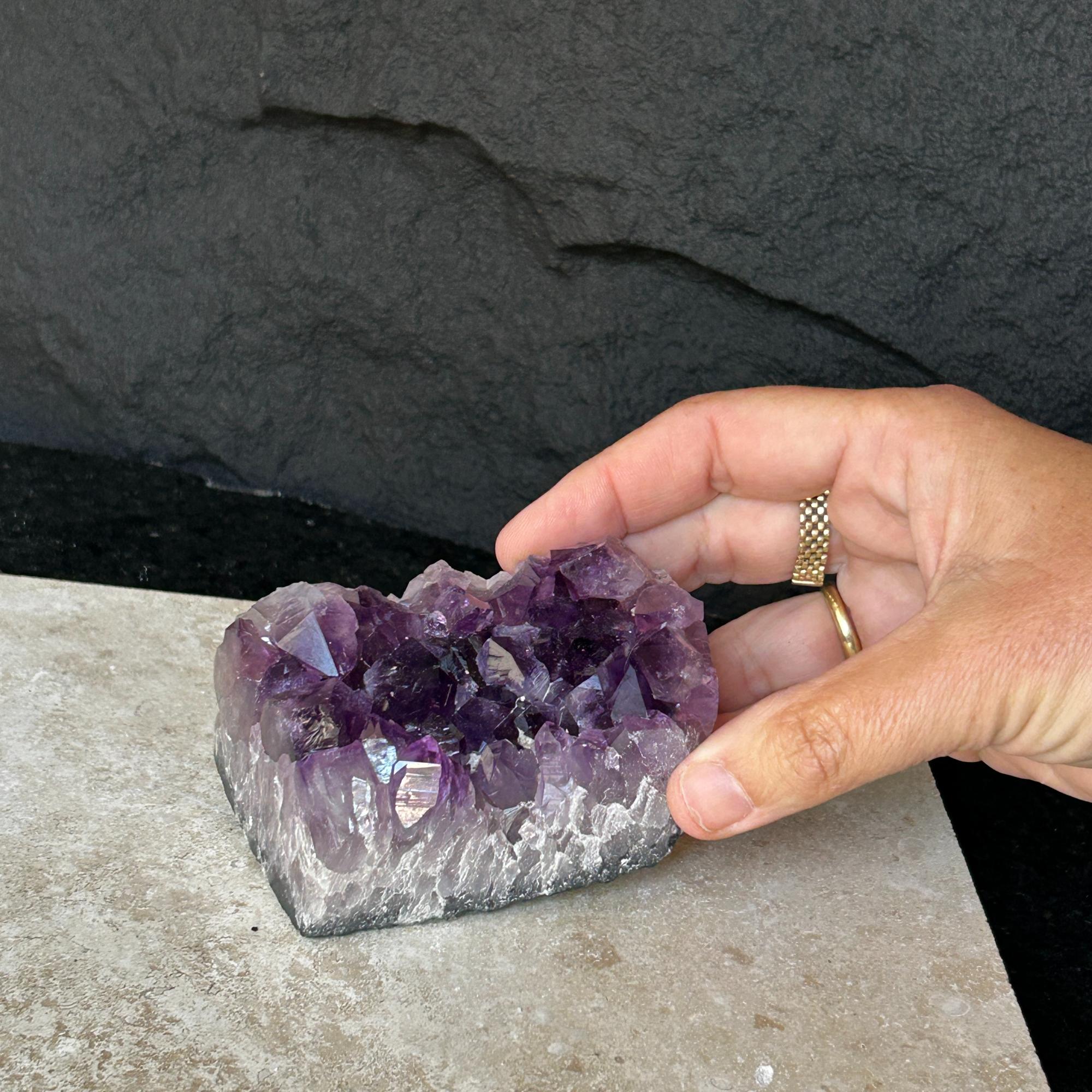 Hand holding a flat, vibrant deep purple Uruguayan amethyst crystal cluster with a raw base.