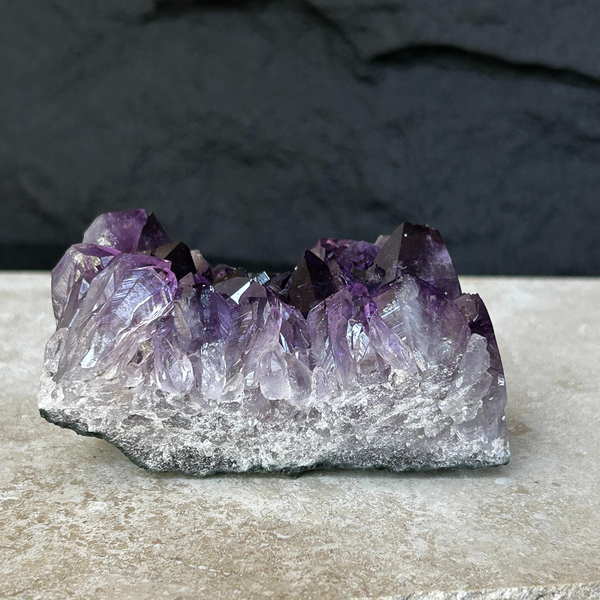 Flat, raw amethyst crystal cluster with vibrant deep purple points and a natural grey base.