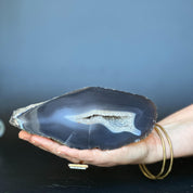 Hand holding a 7-inch dark blue agate geode slice with white crystal cave and bands.