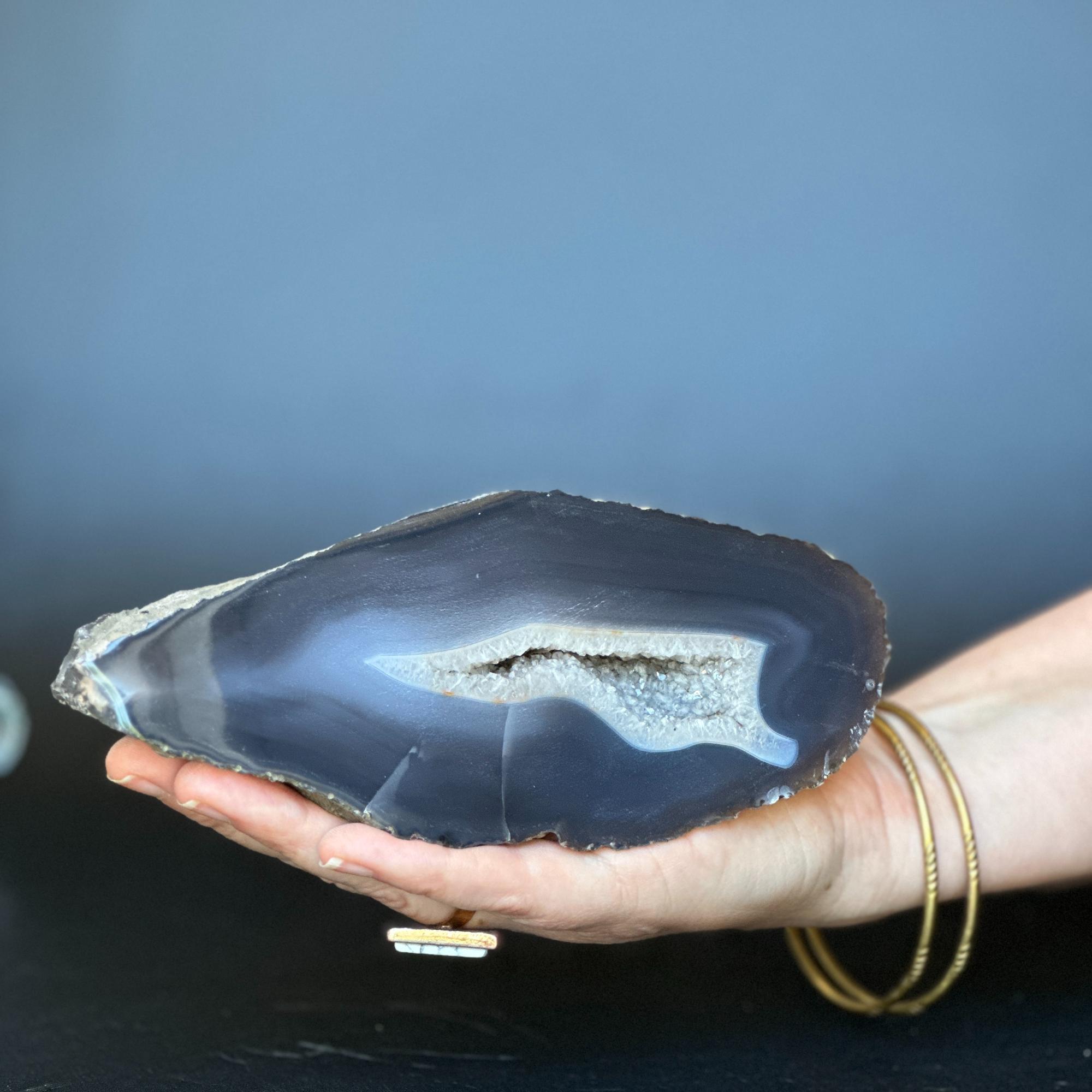Hand holding a 7-inch dark blue agate geode slice with white crystal cave and bands.